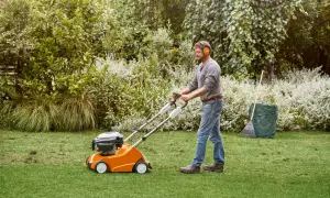 Uomo con cuffie protettive usa un attrezzo per scarificare il prato, rimuovendo feltro e muschio per un prato più sano.