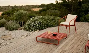 Un elegante patio in legno con mobili rossi, un sentiero di ghiaia e piante mediterranee. Perfetto per idee giardino senza prato.