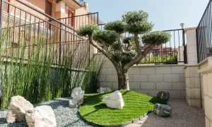 Come arredare un piccolo giardino davanti casa: un ulivo bonsai, erba sintetica, rocce e ghiaia creano un angolo zen.