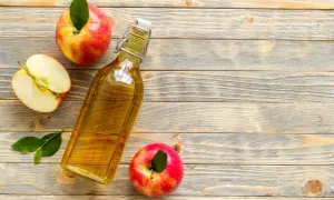 Bottiglia di aceto di mele, mele intere e a metà su fondo di legno. Rimedio naturale contro i parassiti.
