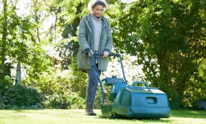 Donna con tosaerba verde, impegnata a tagliare erba bagnata in un giardino soleggiato.