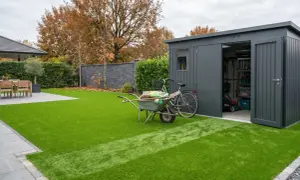 Giardino moderno con prato sintetico impeccabile. Carriola, bici e capanno attrezzi suggeriscono idee per giardini con prato sintetico a bassa manutenzione.