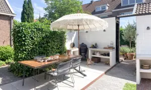 Un'accogliente zona barbecue in giardino con tavolo, sedie, ombrellone e un cane che riposa.