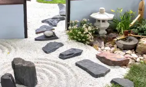 Un sereno giardino zen con ghiaia rastrellata, pietre scure, una lanterna e una fontanella di bambù.