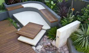 Un elegante giardino moderno con sedute in legno, pavimentazione in ghiaia e una piccola fontana.