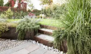 Giardino moderno con gradini in pietra e metallo corten, piante aromatiche rigogliose e ghiaia. Belle idee giardino per un'oasi verde.
