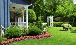 Un giardino fiorito e curato, con un portico blu e un gazebo bianco. Un'esplosione di colori dove non cresce erba, con aiuole piene di fiori rossi e bianchi.