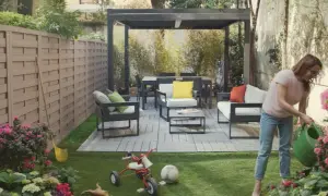 Donna annaffia fiori in un giardino moderno con mobili da esterno e un pergolato. Giardini idee da copiare per un'oasi urbana.