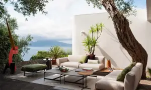 Arredare un terrazzo scoperto con divani chiari, tavolini moderni e piante rigogliose, con vista mare.