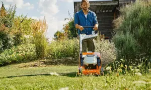 Uomo con tosaerba elettrico su un prato verde, con fiori e vegetazione rigogliosa. Un perfetto prato primavera.