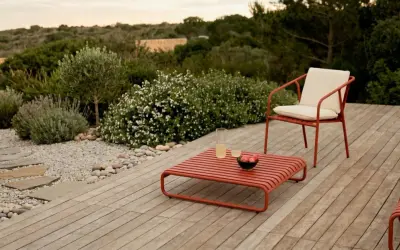 Un elegante patio in legno con mobili rossi, un sentiero di ghiaia e piante mediterranee. Perfetto per idee giardino senza prato.