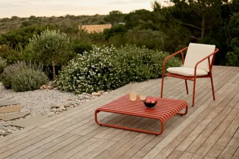 Un elegante patio in legno con mobili rossi, un sentiero di ghiaia e piante mediterranee. Perfetto per idee giardino senza prato.