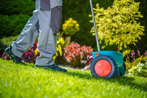 Un giardiniere sparge il fertilizzante con uno spargisemi, preparando il prato per la primavera. Il gramignone in inverno è dormiente, ma ora è il momento di nutrirlo.