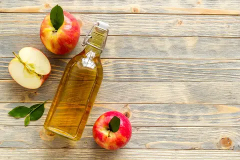 Bottiglia di aceto di mele, mele intere e a metà su fondo di legno. Rimedio naturale contro i parassiti.