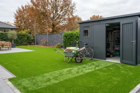 Giardino moderno con prato sintetico impeccabile. Carriola, bici e capanno attrezzi suggeriscono idee per giardini con prato sintetico a bassa manutenzione.
