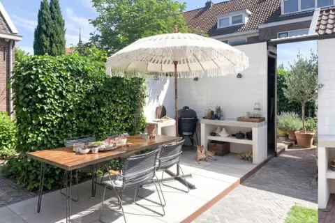 Un'accogliente zona barbecue in giardino con tavolo, sedie, ombrellone e un cane che riposa.