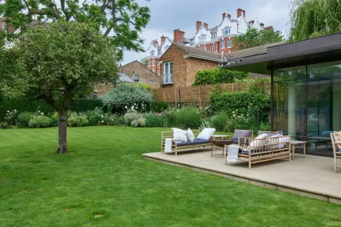 Un'oasi verde perfetta per chi ama progettare giardino. Un prato curato, un patio con mobili in bambù e una vista su edifici storici.
