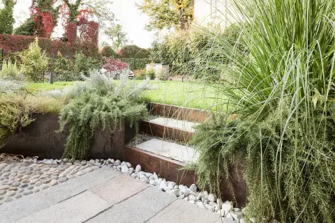 Giardino moderno con gradini in pietra e metallo corten, piante aromatiche rigogliose e ghiaia. Belle idee giardino per un'oasi verde.