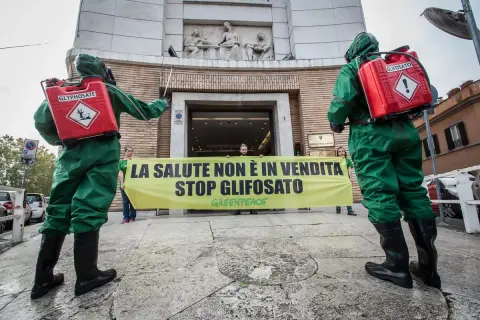 Due persone in tute protettive con bombole di glifosato protestano contro il suo uso, ricordando che il diserbante è pericoloso per l'uomo.