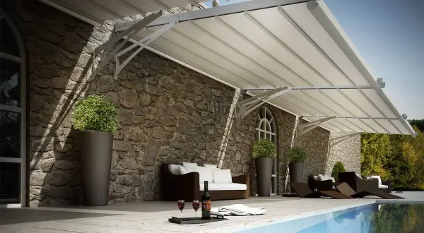 Tettoia addossata moderna su muro in pietra, con divano, sdraio e piscina.