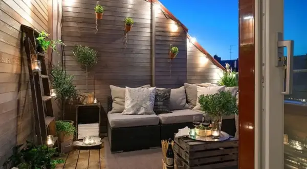 Accogliente terrazza con divanetto, luci soffuse e piante. Idee decorazioni giardino fai da te con scale vintage e cassette di legno.