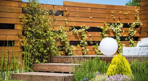 Moderna recinzione in legno con rampicanti fioriti, perfetta come idee per recinzioni esterne fai da te. Un giardino zen con luci e arredi.
