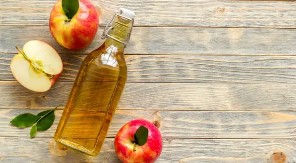 Bottiglia di aceto di mele, mele intere e a metà su fondo di legno. Rimedio naturale contro i parassiti.