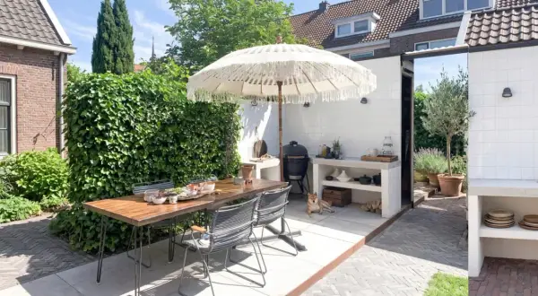 Un'accogliente zona barbecue in giardino con tavolo, sedie, ombrellone e un cane che riposa.
