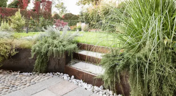 Giardino moderno con gradini in pietra e metallo corten, piante aromatiche rigogliose e ghiaia. Belle idee giardino per un'oasi verde.