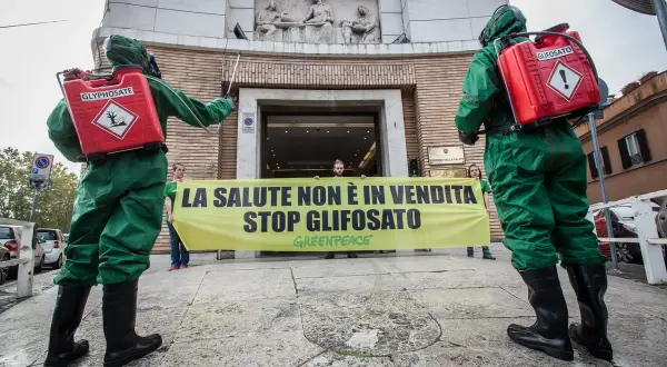 Due persone in tute protettive con bombole di glifosato protestano contro il suo uso, ricordando che il diserbante è pericoloso per l'uomo.