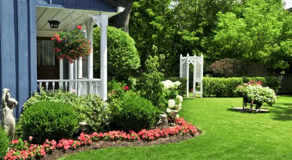 Un giardino fiorito e curato, con un portico blu e un gazebo bianco. Un'esplosione di colori dove non cresce erba, con aiuole piene di fiori rossi e bianchi.