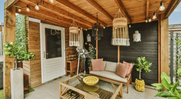 Un portico accogliente con divano, tavolino in legno e vetro, piante e decorazioni boho. Idee per come abbellire un portico con stile.