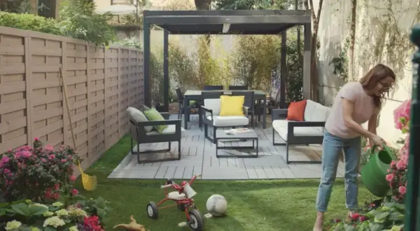 Donna annaffia fiori in un giardino moderno con mobili da esterno e un pergolato. Giardini idee da copiare per un'oasi urbana.