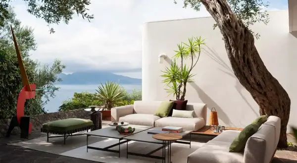 Arredare un terrazzo scoperto con divani chiari, tavolini moderni e piante rigogliose, con vista mare.