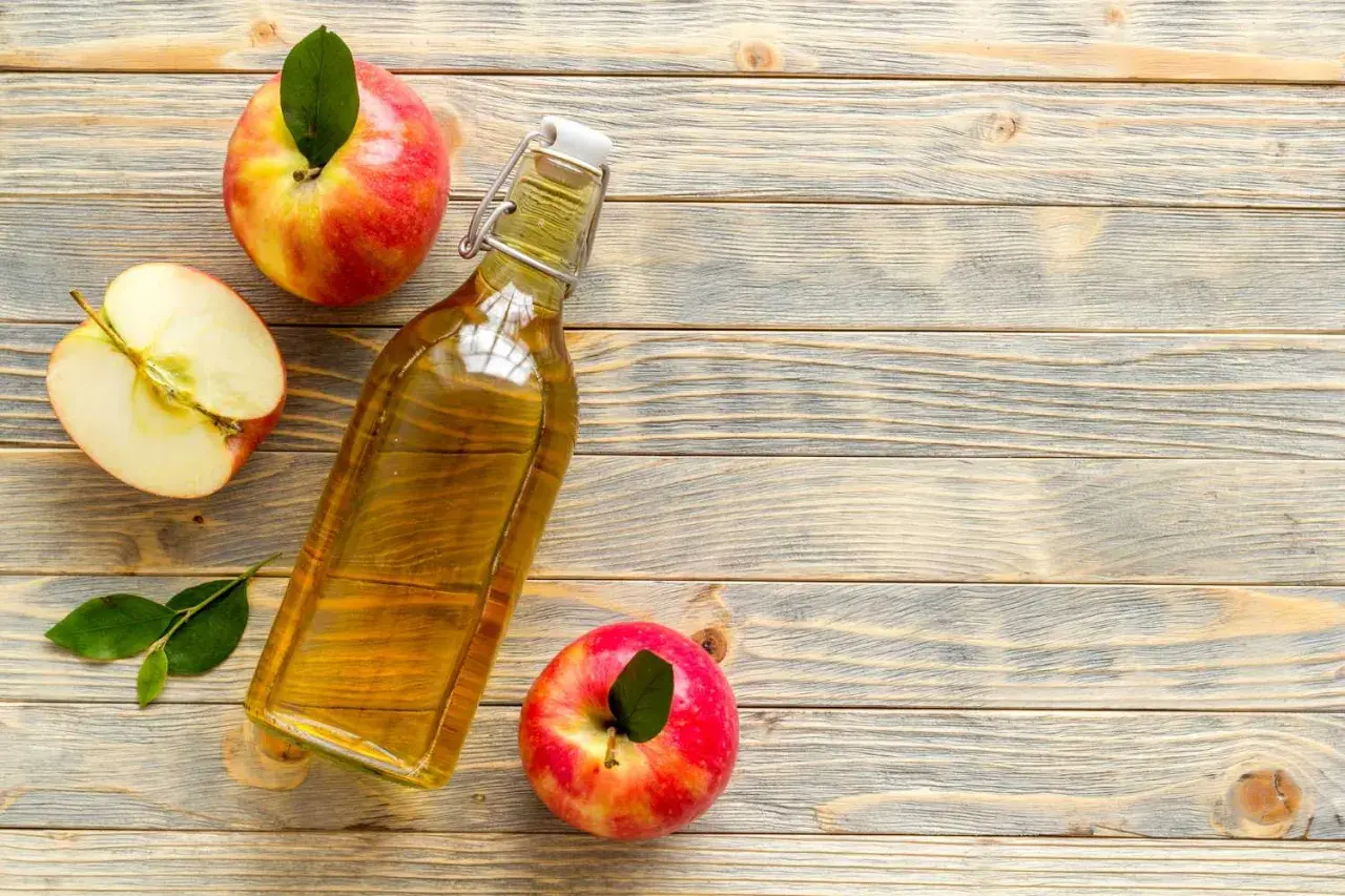 Bottiglia di aceto di mele, mele intere e a metà su fondo di legno. Rimedio naturale contro i parassiti.