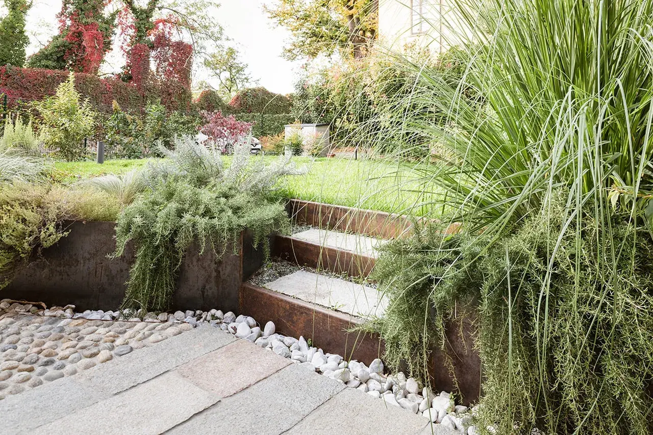 Giardino moderno con gradini in pietra e metallo corten, piante aromatiche rigogliose e ghiaia. Belle idee giardino per un'oasi verde.
