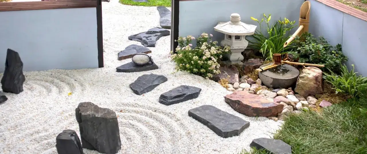 Un sereno giardino zen con ghiaia rastrellata, pietre scure, una lanterna e una fontanella di bambù.