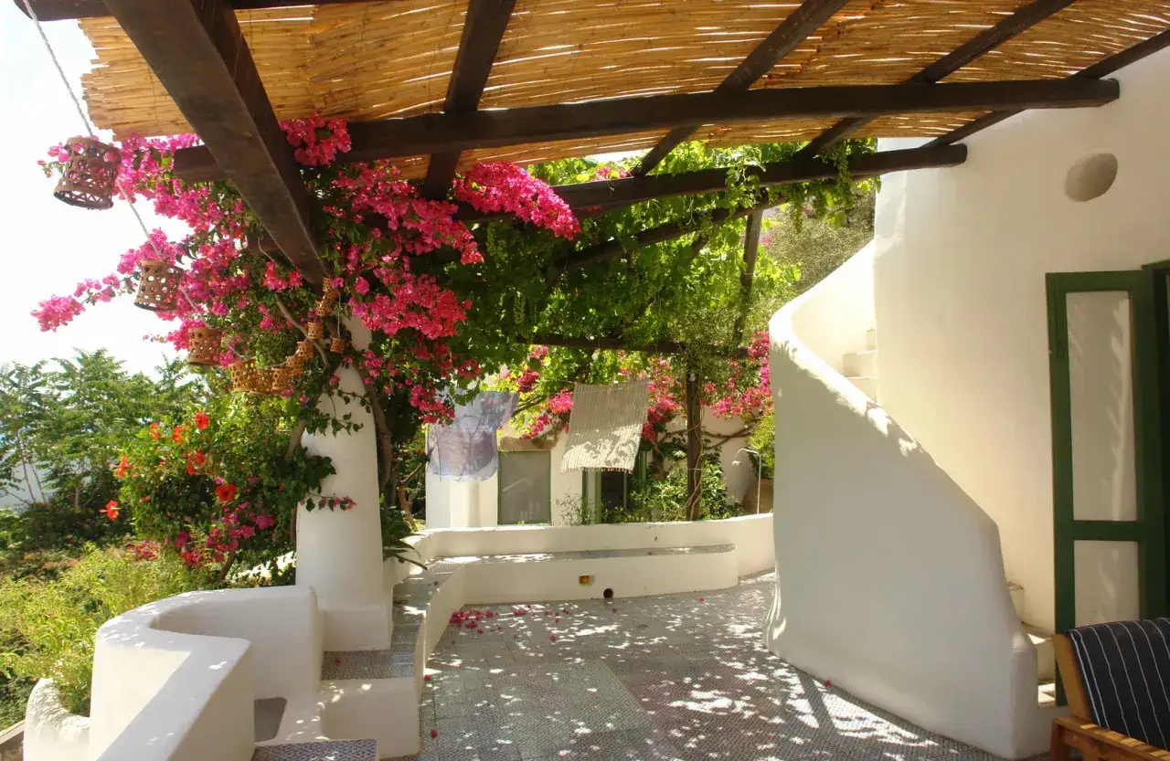 Un portico fiorito con bouganville rosa e lanterne di bambù. Un esempio di come abbellire un portico con piante e decorazioni naturali.