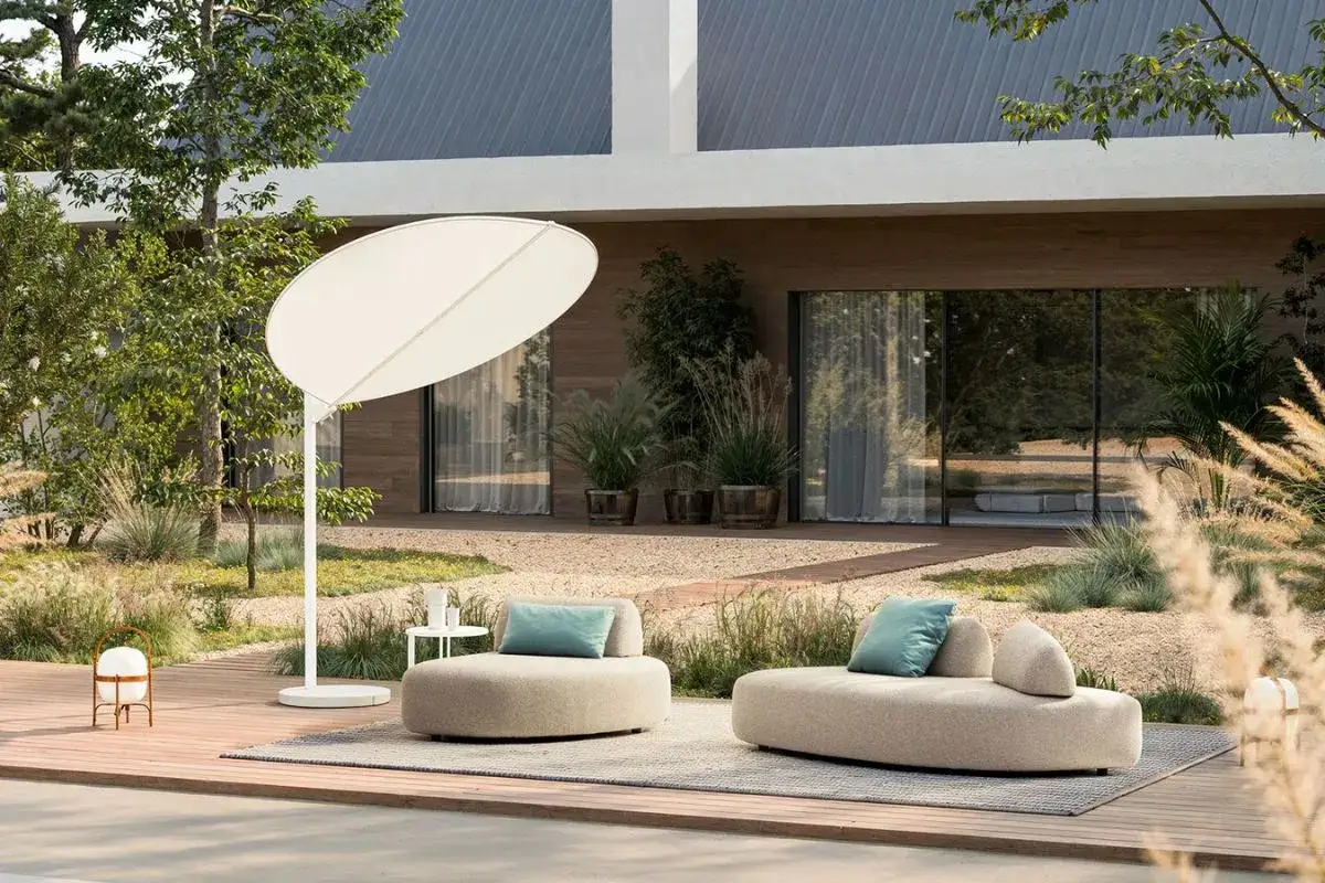 Arredo esterno per giardini moderni minimal: divani curvi, ombrellone bianco e lampada da terra su un deck in legno.