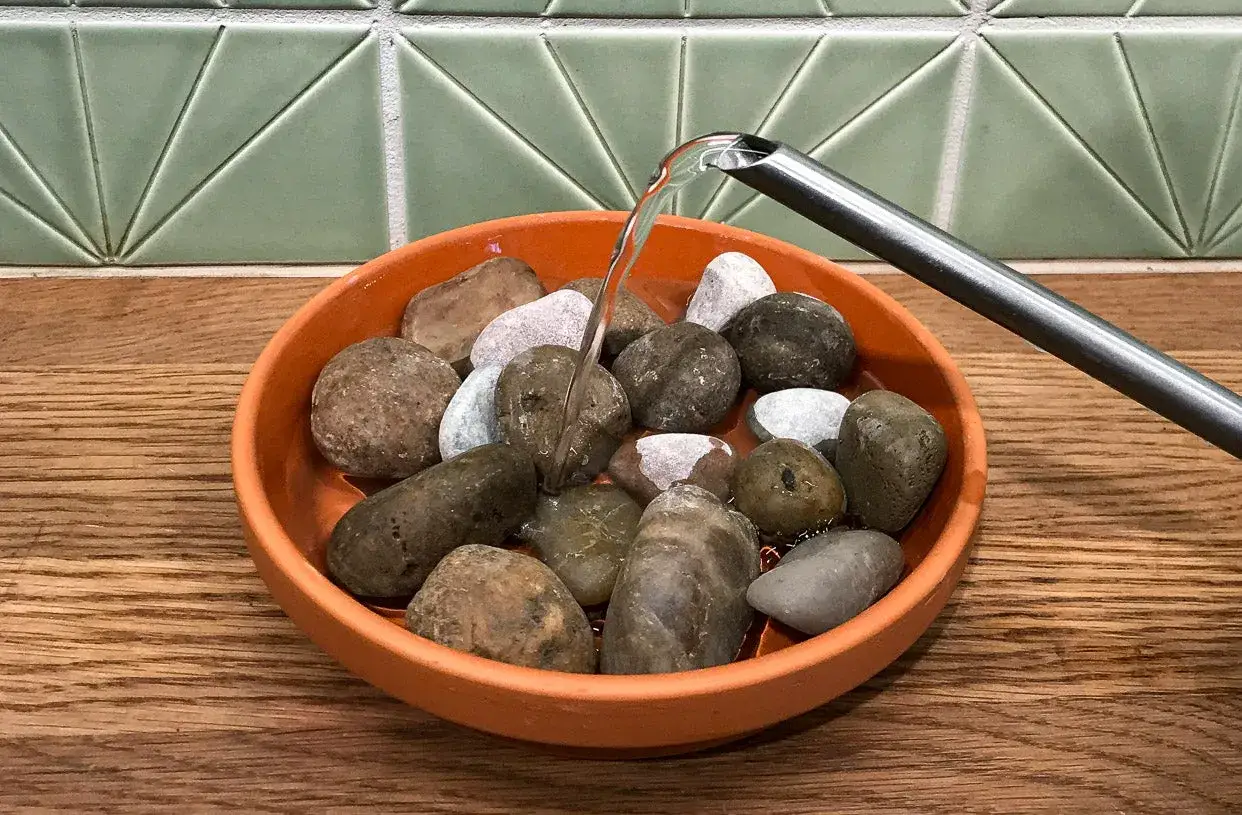 Acqua versata su ciottoli in un sottovaso arancione, un metodo per creare umidità per le piante.