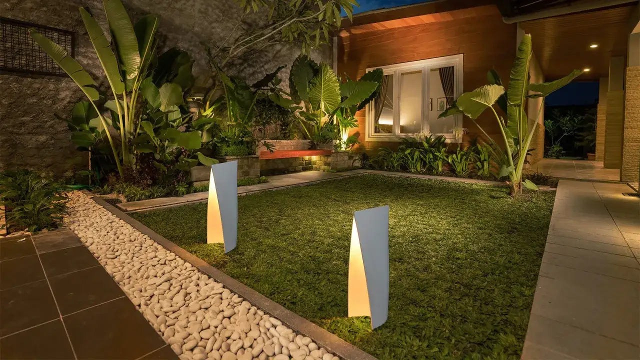 Un giardino illuminato con luci moderne e piante rigogliose per abbellire l'ingresso esterno casa.