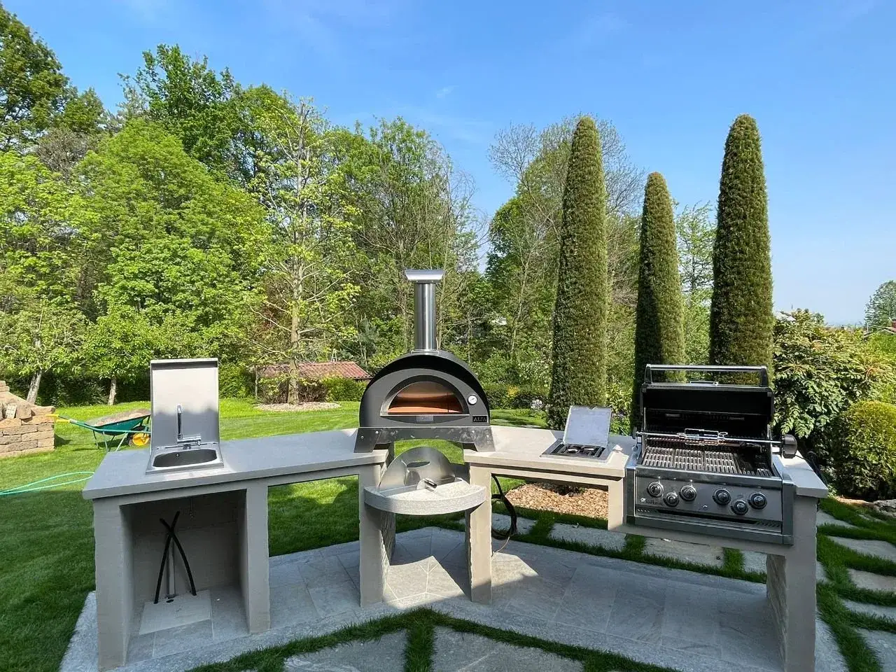 Una splendida zona barbecue in giardino con forno a legna, grill e lavandino, pronta per grigliate estive.