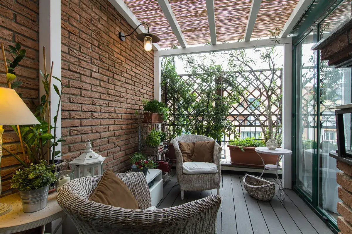 Veranda piccola arredata con mobili in vimini, piante e luci soffuse. Un esempio di come arredare una veranda piccola con stile e comfort.