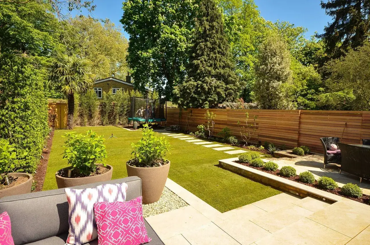 Esempio progetto giardino moderno con prato curato, vasi grandi, patio in pietra e trampolino per bambini.