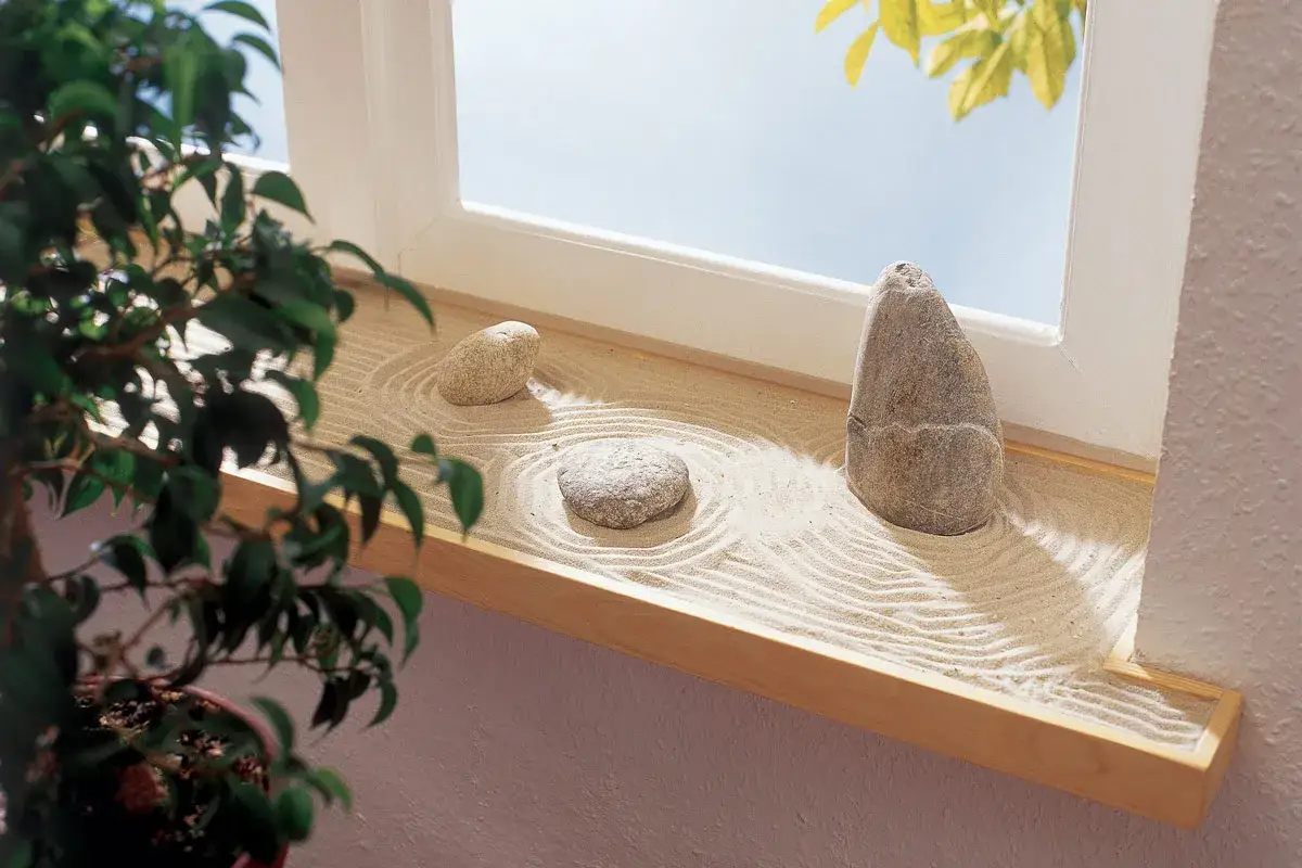 Un piccolo giardino zen sul davanzale, con sabbia rastrellata e tre pietre che invitano alla meditazione.