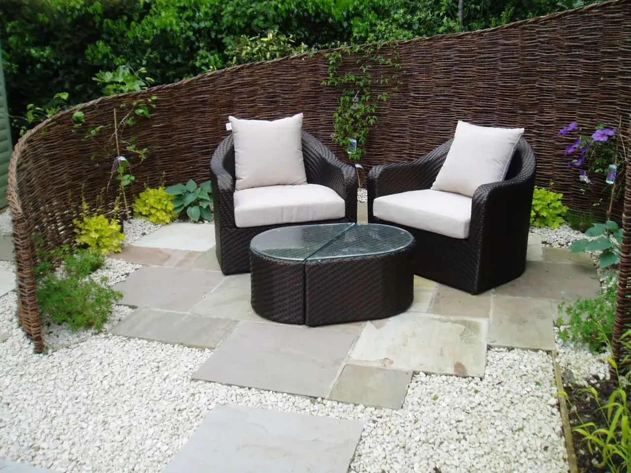 Un angolo relax con mobili in rattan e tavolino in vetro, circondato da ghiaia bianca e lastre di pietra: cosa mettere dove non cresce erba per un giardino curato.