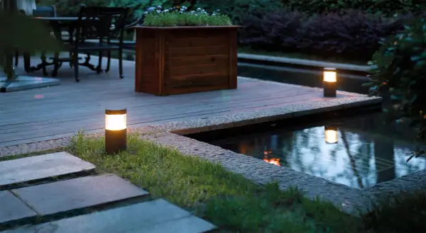 Illuminazione da giardino: lanterne moderne creano un'atmosfera magica lungo il laghetto e il patio in legno.