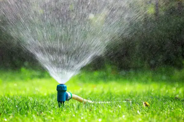 Irrigatore blu in azione su un prato verde brillante, un segnale visivo di quando innaffiare il prato per mantenerlo rigoglioso.