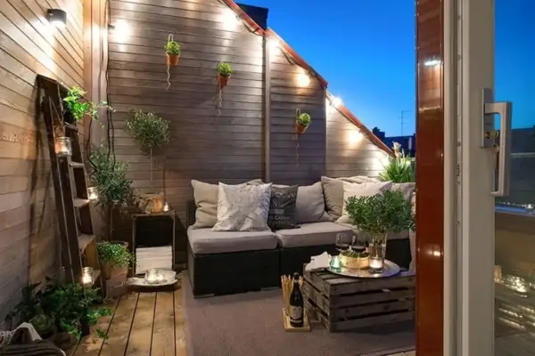 Accogliente terrazza con divanetto, luci soffuse e piante. Idee decorazioni giardino fai da te con scale vintage e cassette di legno.