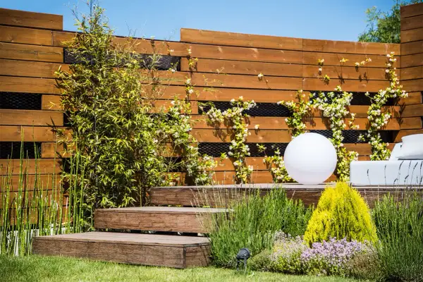 Moderna recinzione in legno con rampicanti fioriti, perfetta come idee per recinzioni esterne fai da te. Un giardino zen con luci e arredi.